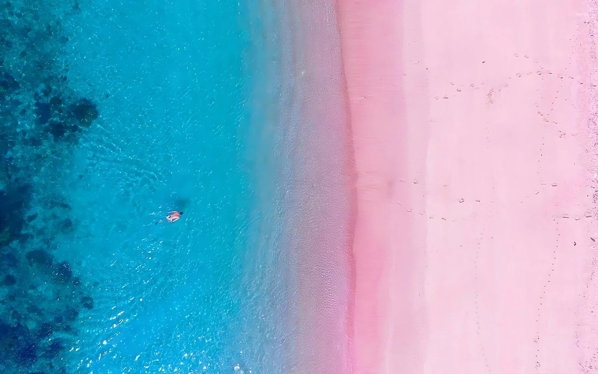 A curve of pale pink sand with a wooden boat anchored in shallow turquoise water