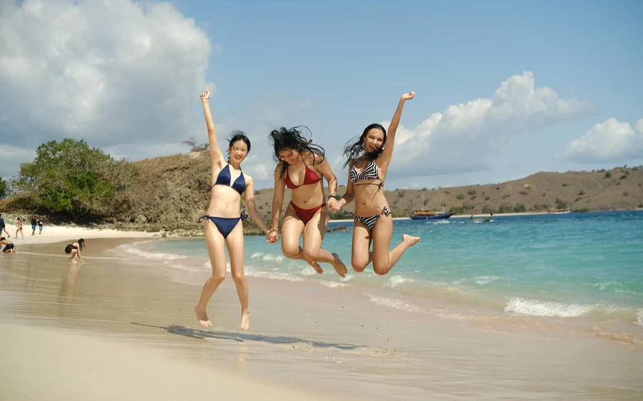 Three travellers jumping on a beach beside turquoise water