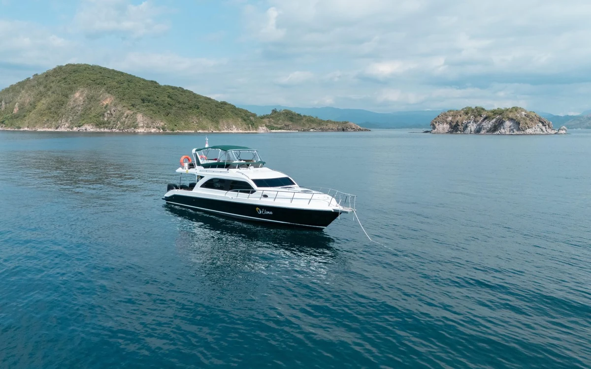 A white speedboat on calm water between two low green islands